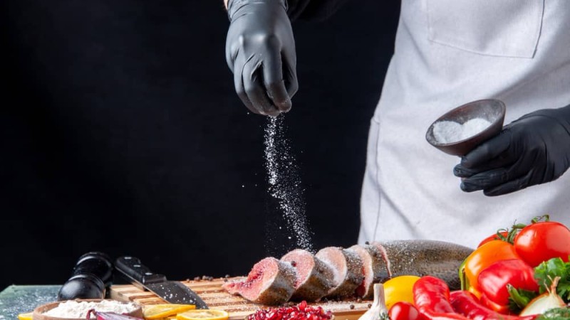 front-view-chef-sprinkled-flour-raw-fish-slices-cutting-board-vegetables-wood-serving-board-knife-kitchen-table